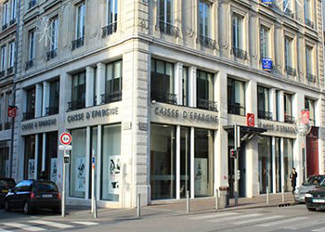 Façade d'une agence Caisse d'Epargne au rez-de-chaussée d'un grand immeuble haussmannien en pierre claire, à l'angle d'une rue.