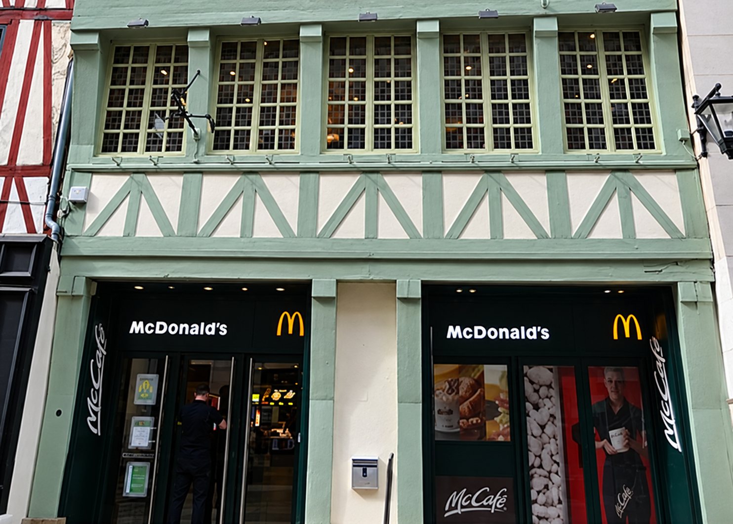 Façade d'un restaurant McDonald's installé au rez-de-chaussée d'un immeuble ancien à colombages peint en vert, avec deux entrées vitrées et le logo aux arches dorées.