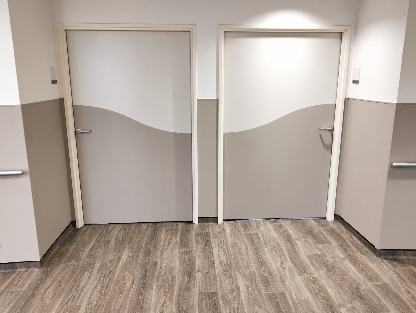 Deux portes grises et blanches à motif ondulé dans un couloir aux murs bicolores, avec barres d'appui et sol imitation parquet.